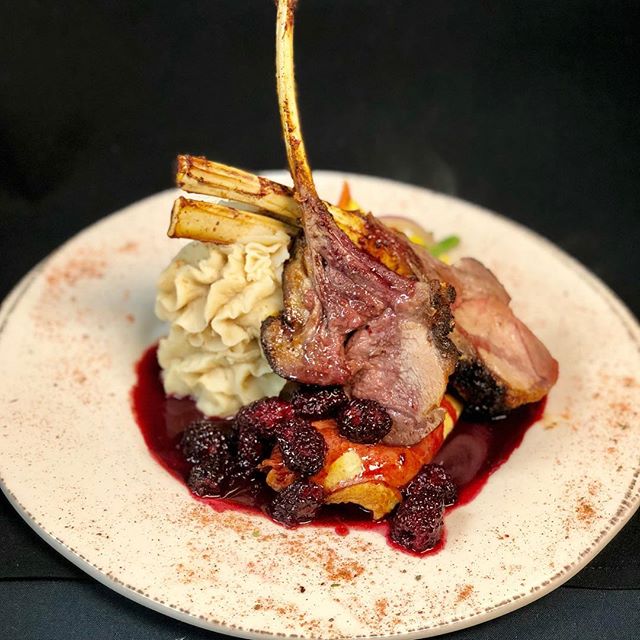 A plate of lamb with mashed potatoes and berries.