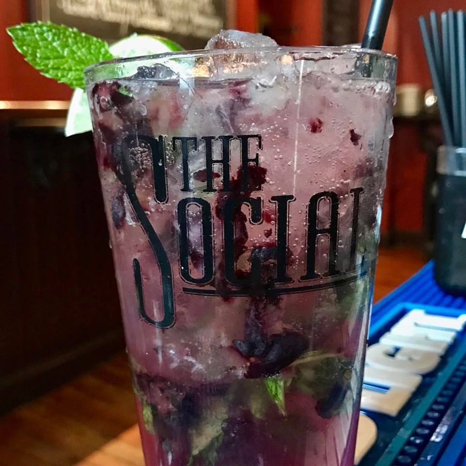 A drink with blueberries and mint on top of a bar.