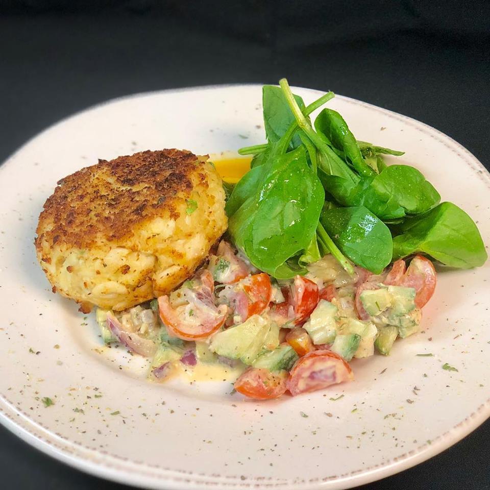 A plate with a crab cake and salad on it.